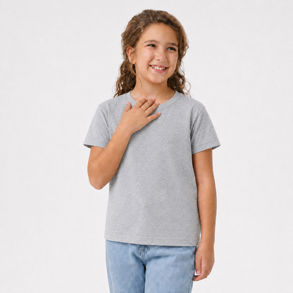 A young girl with curly brown hair smiling, wearing a light gray short-sleeve crewneck t-shirt and light blue jeans, standing against a solid white studio background.