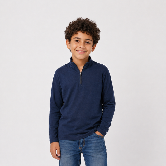 A young boy with curly brown hair wearing a navy blue long-sleeve quarter-zip pullover and blue jeans, standing against a light gray studio background.
