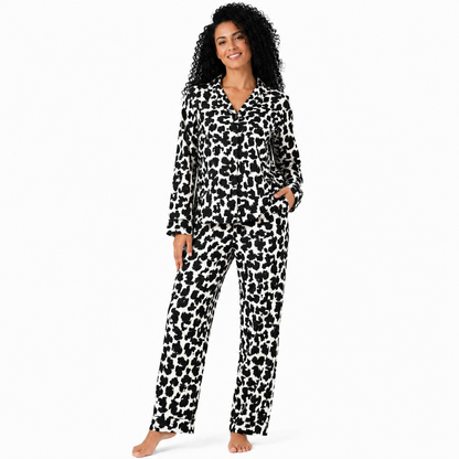 A woman modeling a black and white cow-print pajama set with a long-sleeve button-up top and matching pants, photographed against a solid white background.
