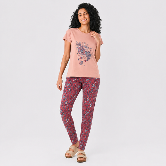 A woman modeling a two-piece loungewear set consisting of a dusty pink t-shirt with a paisley graphic and matching red floral print leggings, set against a plain light gray background.