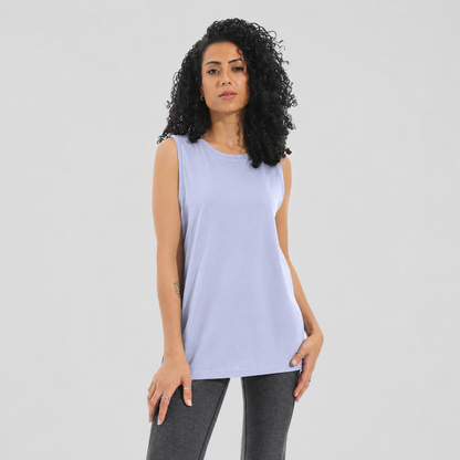 A woman with curly black hair wearing a sleeveless light lavender tank top and dark gray leggings, standing against a solid light gray background.