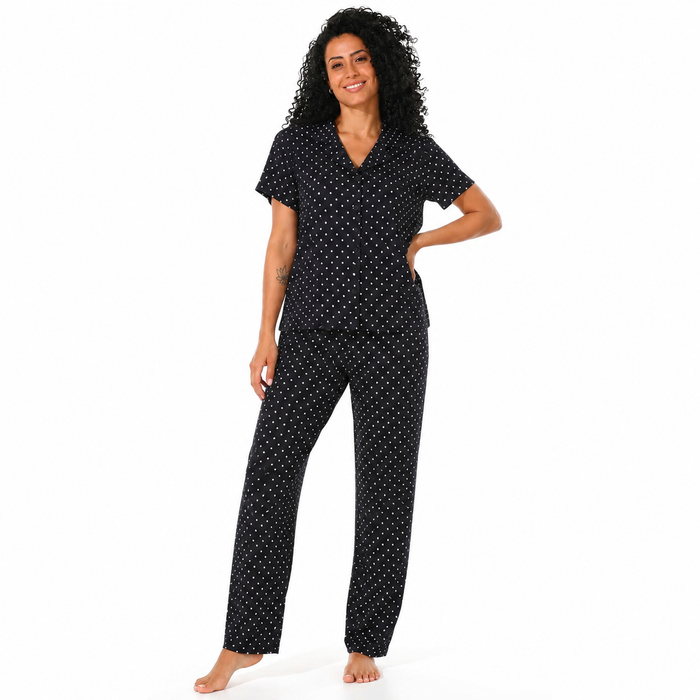 A woman modeling a two-piece pajama set consisting of a short-sleeve V-neck top and matching pants, both in black with a small white polka dot pattern, against a plain white background.