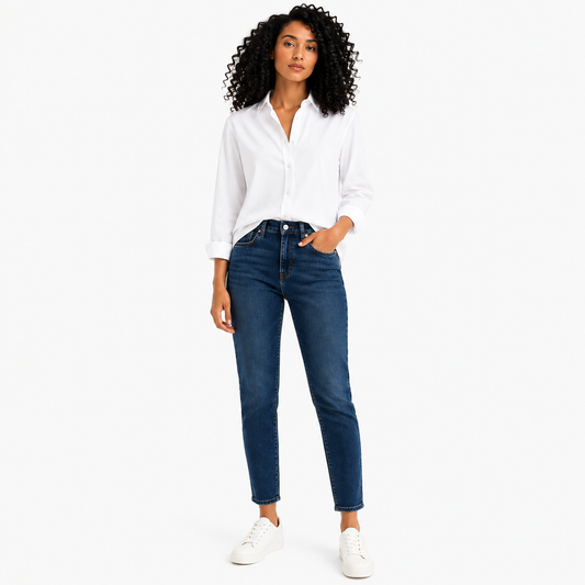 A woman modeling a white long-sleeve button-up shirt and dark blue straight-leg jeans with white sneakers, standing against a plain white studio background.