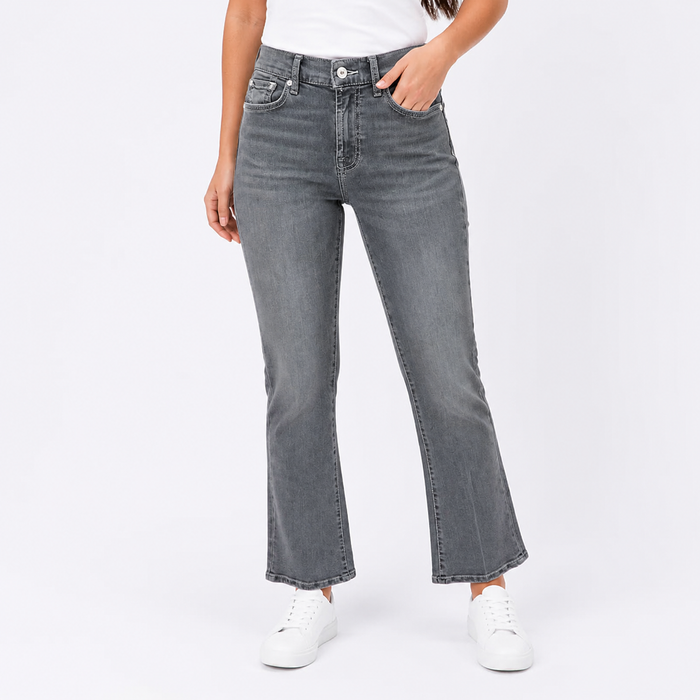 A model wearing a pair of dark gray, straight-leg flared jeans with a faded wash, paired with a white t-shirt and white sneakers, shown from the waist down on a light gray studio background.