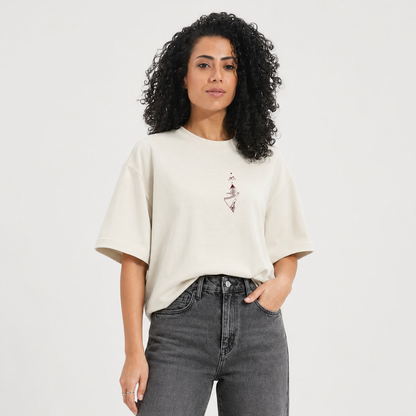 Woman wearing a beige t-shirt with a graphic design and gray jeans on a white background