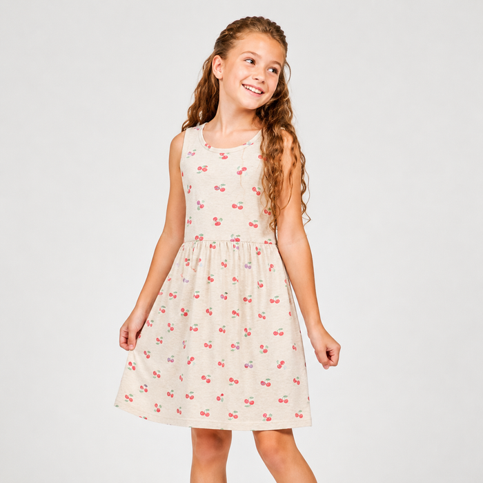Young girl wearing a sleeveless dress with cherry pattern on a plain background