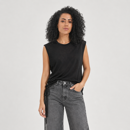 Woman wearing a black sleeveless top and gray jeans on a light gray background