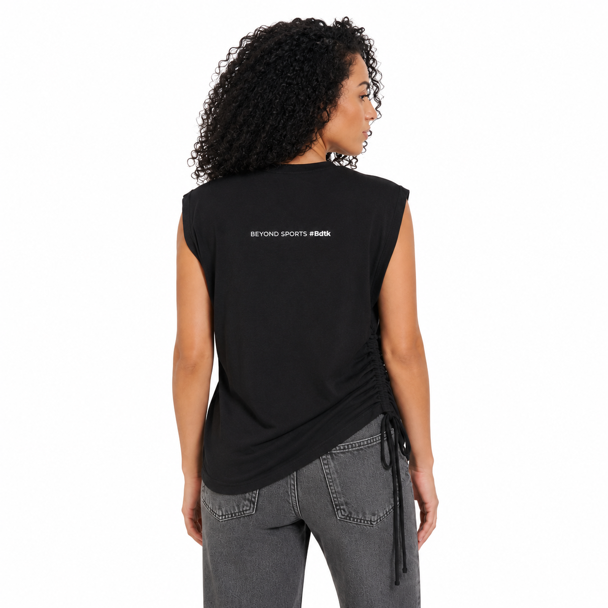 Woman wearing a black sleeveless top with text on the back, standing against a white background