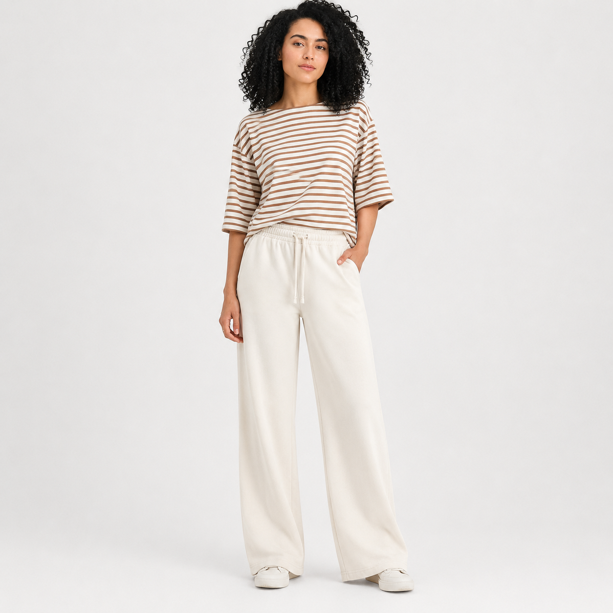 Woman wearing a striped shirt and white pants on a plain background