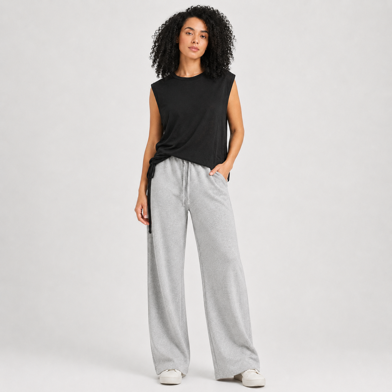 Woman wearing a black sleeveless top and gray wide-leg pants on a white background