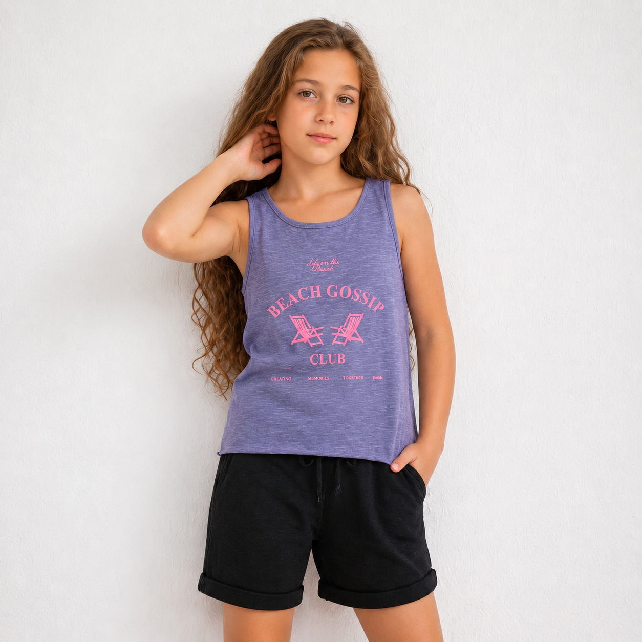 Young girl wearing a purple tank top with 'Beach Gossip Club' text and black shorts on a white background