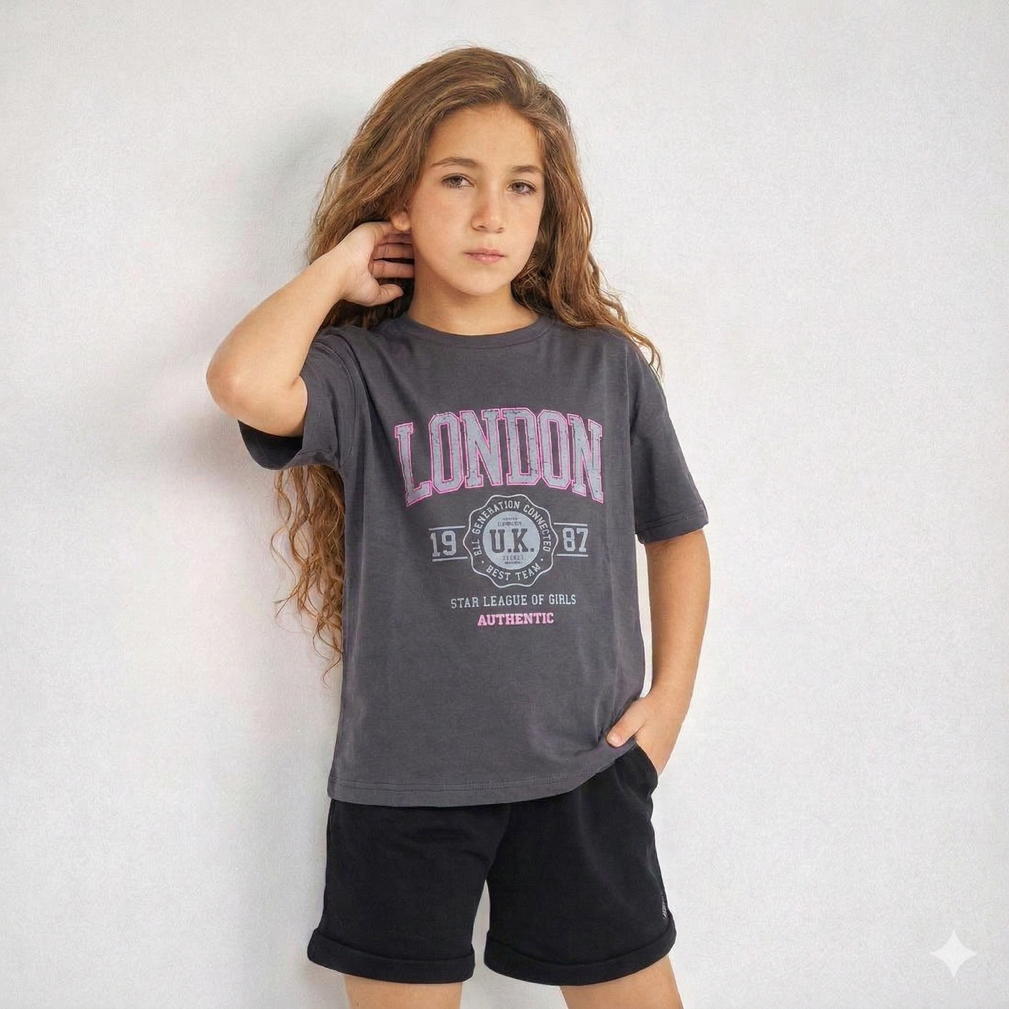 Young girl wearing a gray 'London' t-shirt with black shorts against a white background