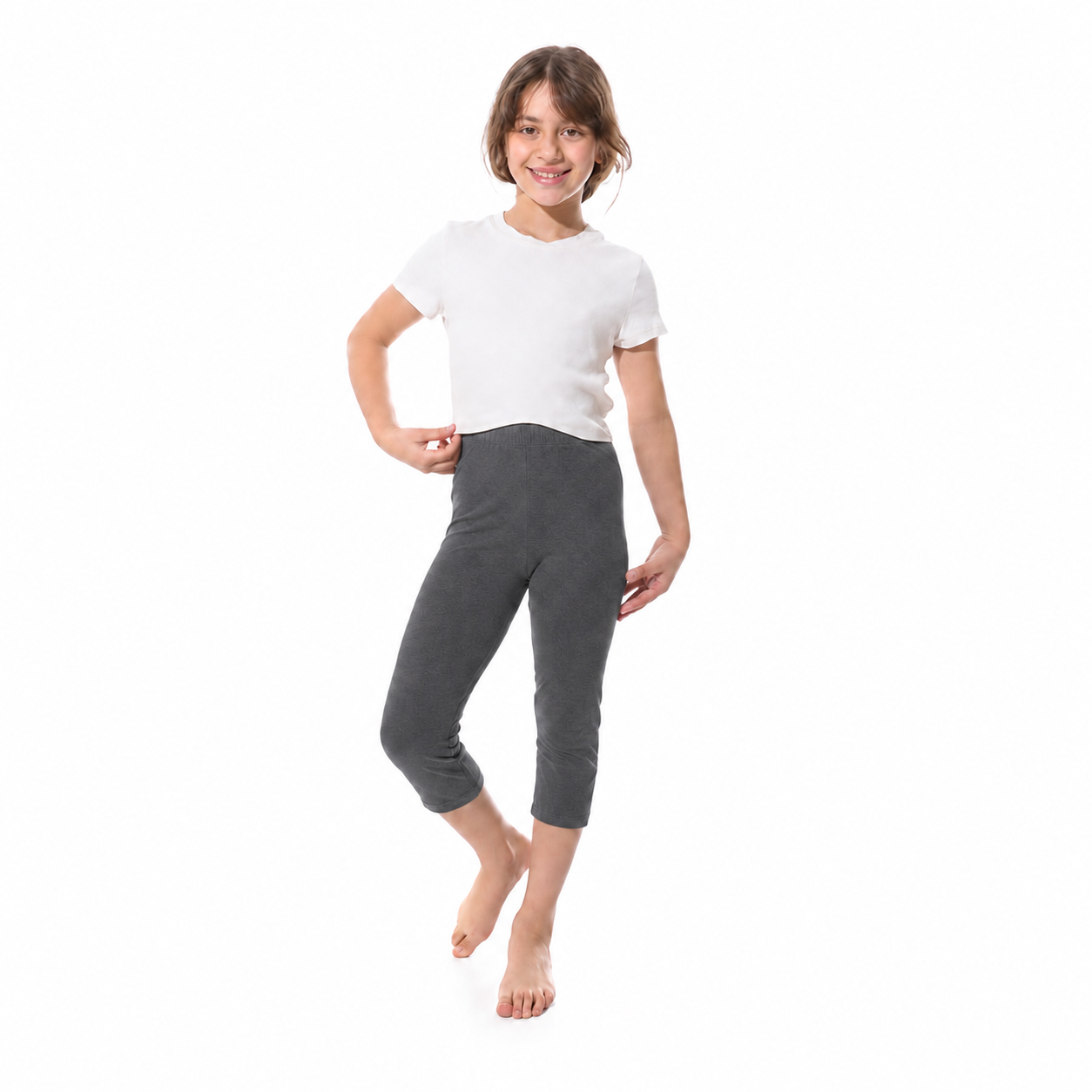 A young girl modeling dark gray cropped leggings and a white t-shirt against a solid white background.