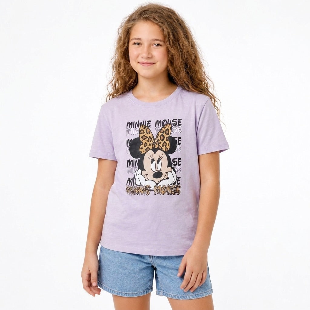 A young girl with long wavy light brown hair wearing a light purple short-sleeve t-shirt with a Minnie Mouse graphic and blue denim shorts, standing against a plain white background.