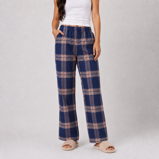 A model wearing blue and beige plaid wide-leg lounge pants, paired with a white tank top and beige slide sandals, standing against a light gray studio background.