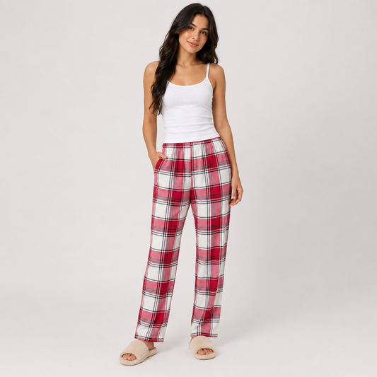 A woman modeling a pair of red, white, and black plaid lounge pants with a white camisole and beige slippers, standing against a light gray studio background.