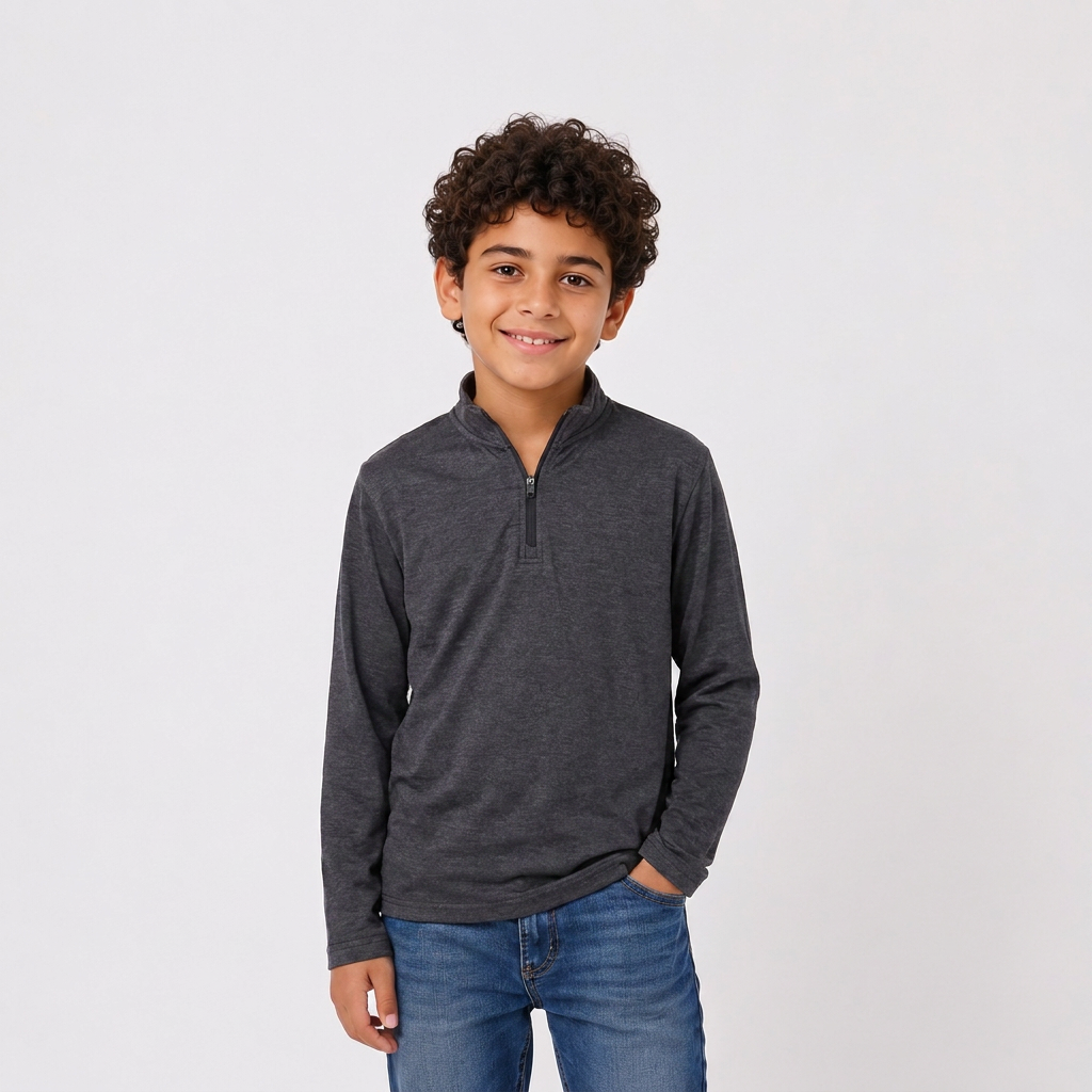 A young boy with curly dark hair wearing a dark gray heathered quarter-zip long-sleeve shirt and blue jeans, standing against a light gray studio background.