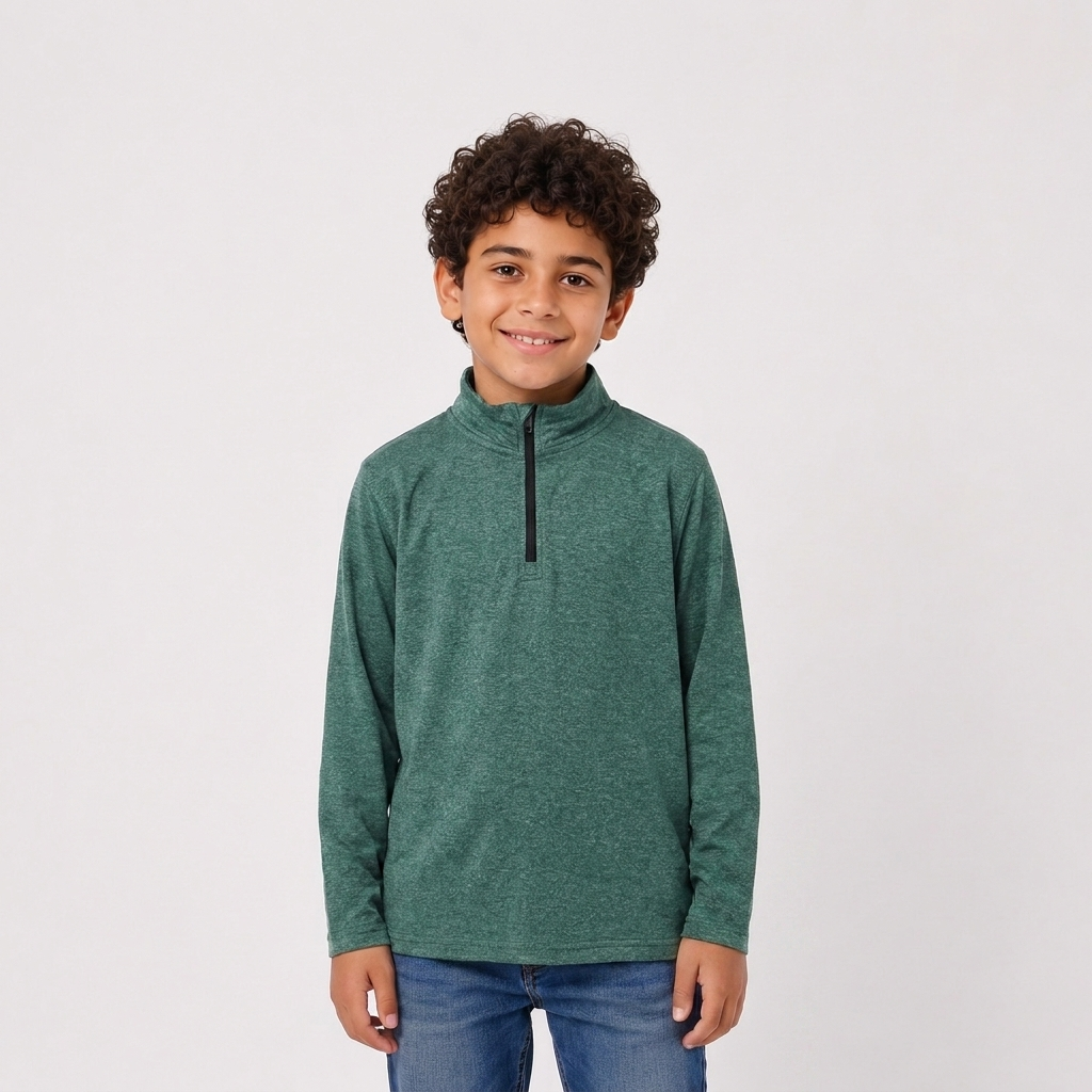 A young boy with curly dark hair stands against a light gray studio background wearing a heathered green long-sleeve quarter-zip pullover and blue jeans.