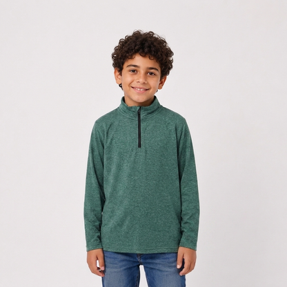 A young boy with curly dark hair stands against a light gray studio background wearing a heathered green long-sleeve quarter-zip pullover and blue jeans.